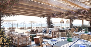 An outdoor seating area with tables and chairs, overlooking a beach.
