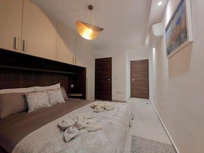Una habitación de hotel con una cama, cabecera, armario, puerta y un cuadro en la pared.