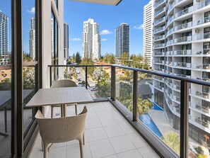 A balcony with a table and chairs, overlooking a cityscape with tall buildings and a clear sky. - City Dreams at Avani | Chic High-Rise Stay (Broadbeach)