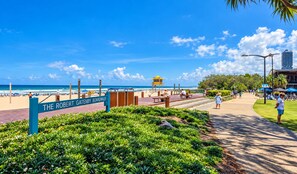 A boardwalk with a sign reading 'The Robert Gatney Boardwalk,' leading to a beach with people and a lifeguard tower. - City Dreams at Avani | Chic High-Rise Stay (Broadbeach)