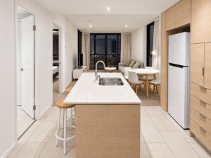 A modern kitchen with a central island, a dining area, and a view of the city at night. - City Dreams at Avani | Chic High-Rise Stay (Broadbeach)