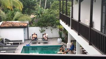 Piscina con sillas de descanso y un área techada con barandilla.