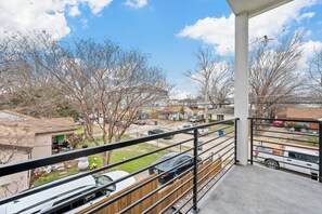 A balcony with a view of a residential street, a parked car, and a clear sky. - Modern 2BR/2.5BA Townhome | 2-Car Garage (Dallas)
