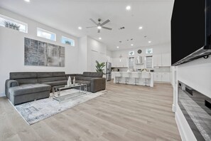 A modern living room with a sectional sofa, a coffee table, and a large painting. - Modern 2BR/2.5BA Townhome | 2-Car Garage (Dallas)
