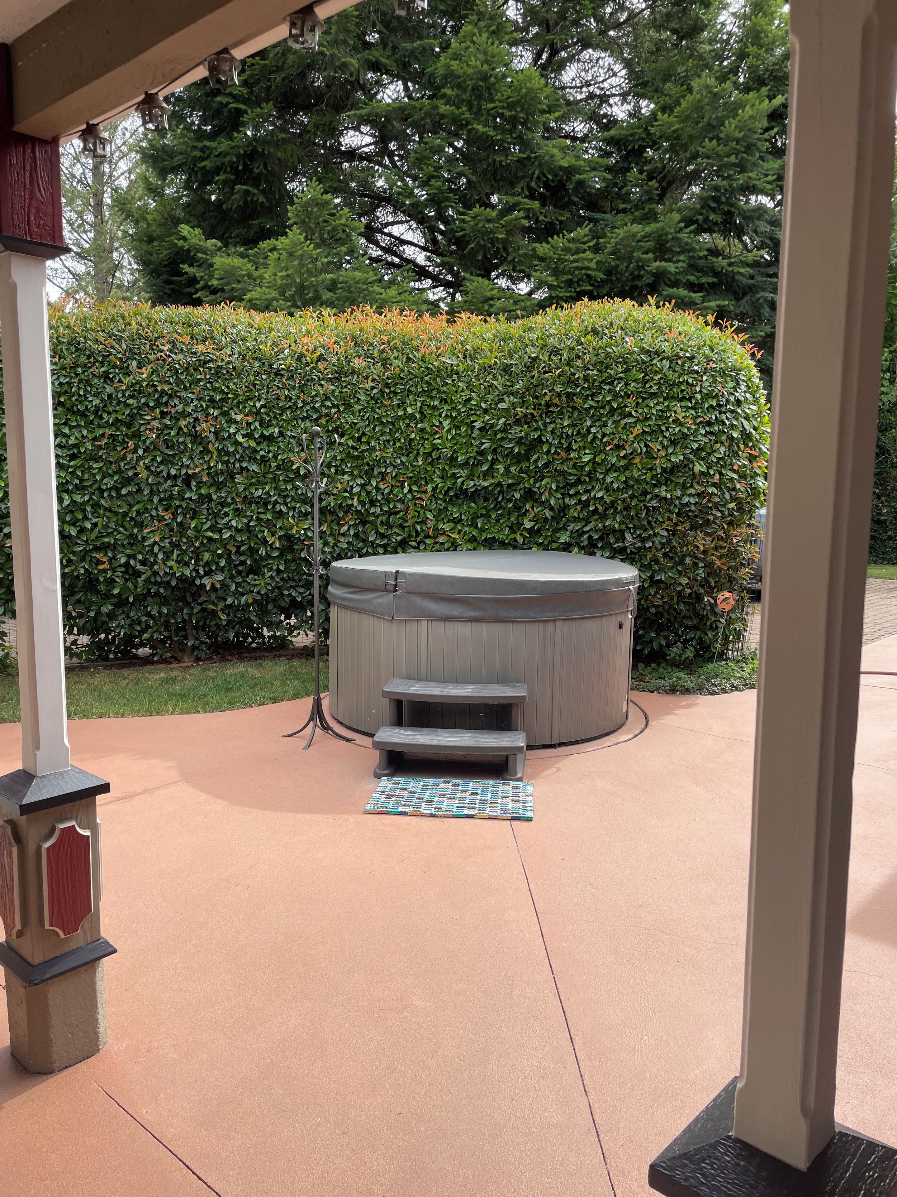 A hot tub with steps, a wooden bench, and a patterned mat on a concrete patio.