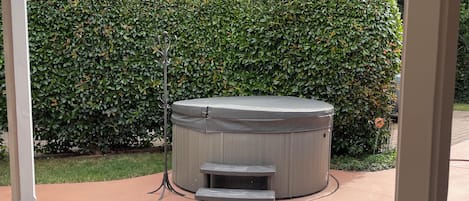 A hot tub with steps, a wooden bench, and a patterned mat on a concrete patio.