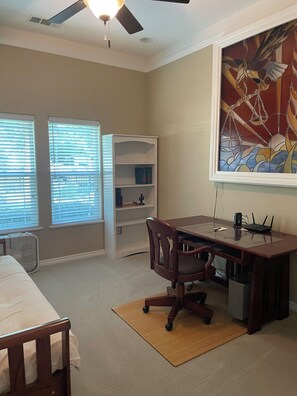 A bedroom with a bed, a desk, a chair, a bookshelf, and a ceiling fan.