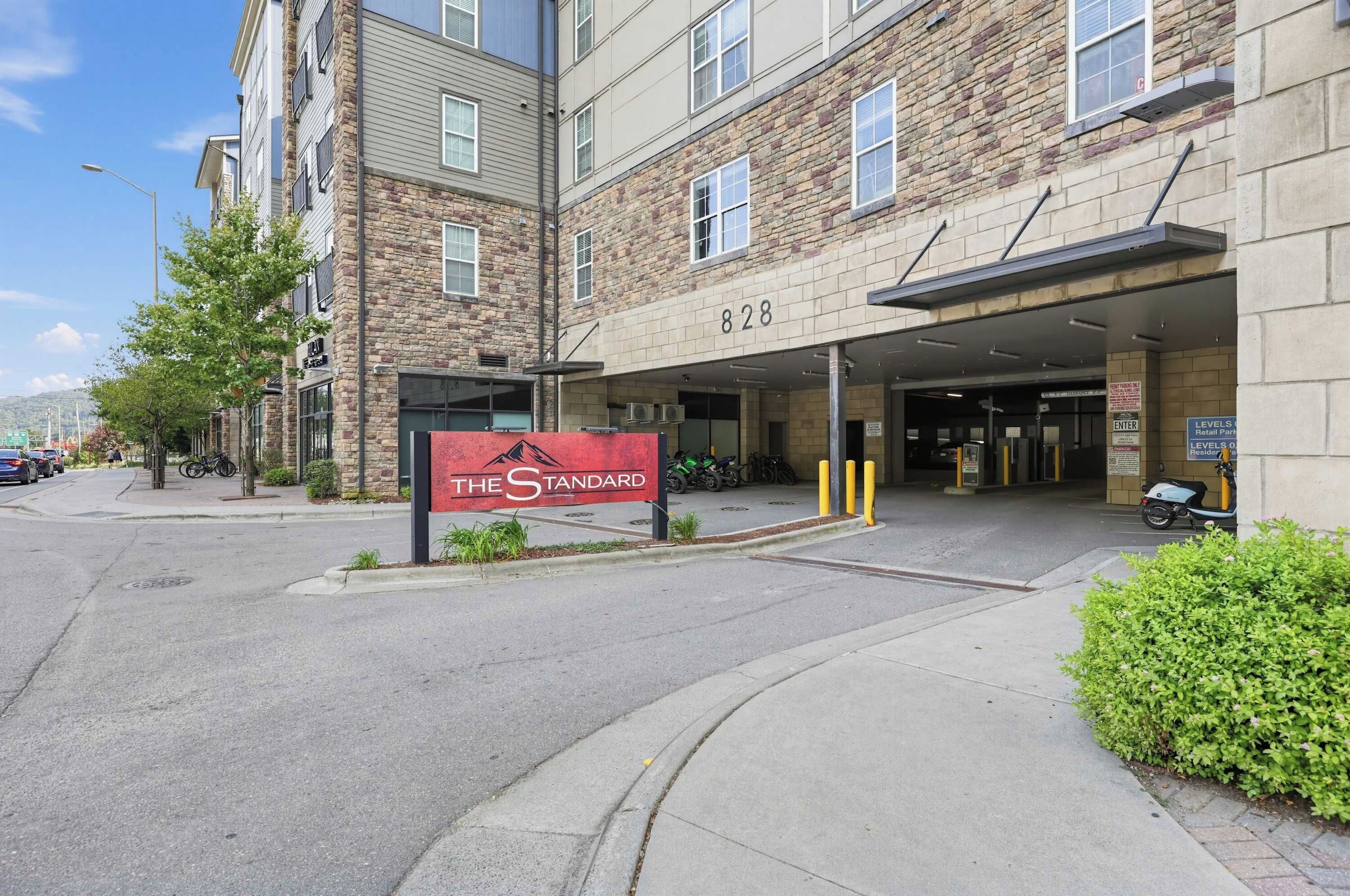 A multi-story building with a stone facade, a sign reading 'The Standard,' and a parking entrance.