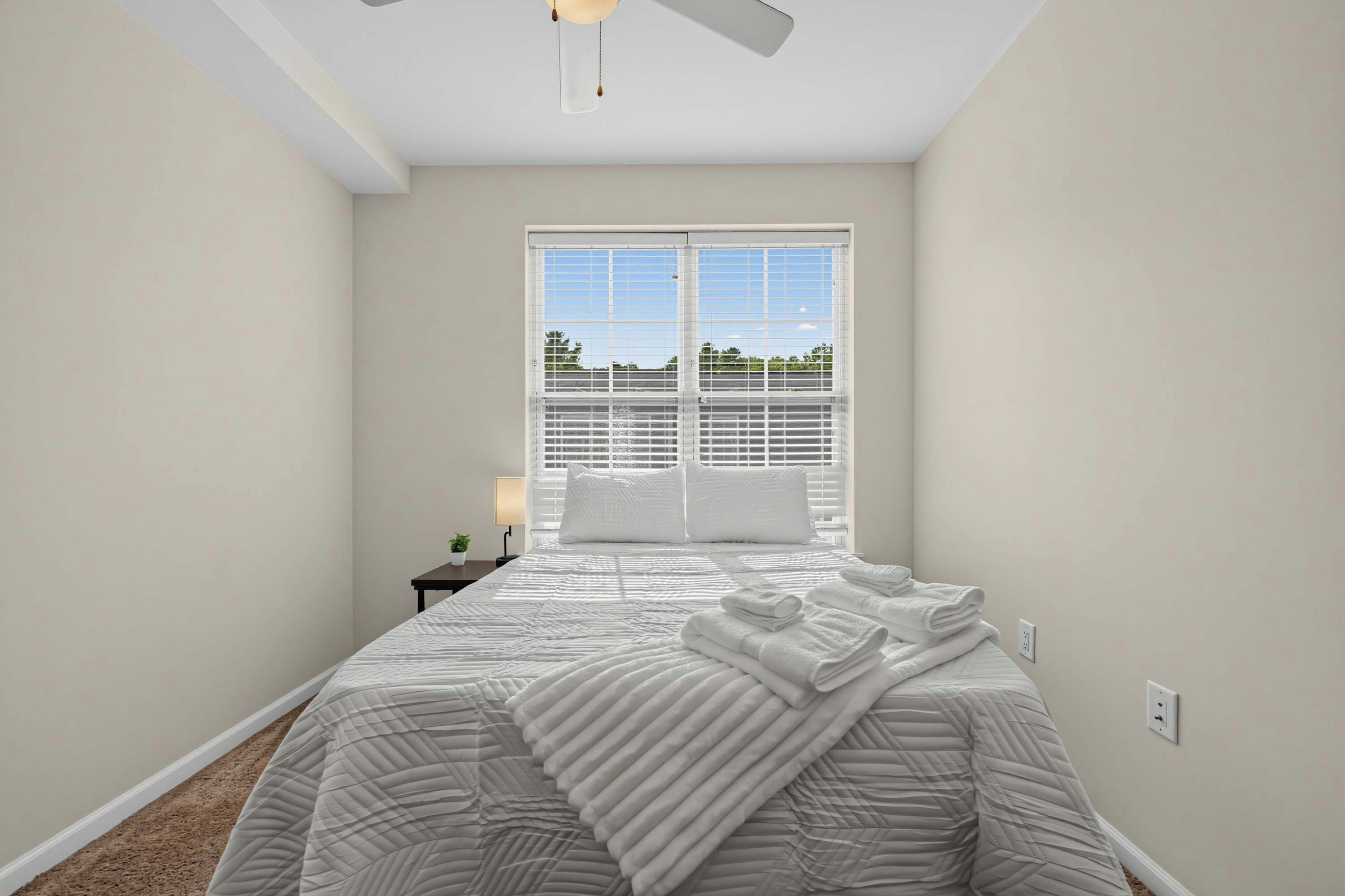 A bedroom with a bed, a nightstand, a lamp, and a window with blinds.