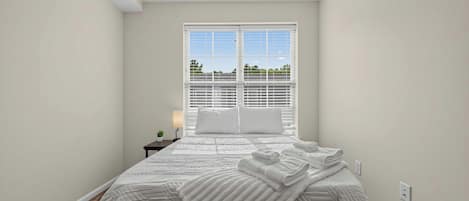A bedroom with a bed, a nightstand, a lamp, and a window with blinds.