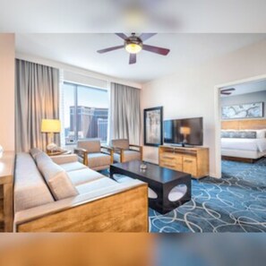 A hotel room with a sofa, a desk, a television, a bed, and a ceiling fan. - Club Wyndham Desert Blue (Las Vegas)