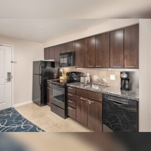 A modern kitchen with dark wooden cabinets, a stainless steel refrigerator, a microwave, and a dishwasher. - Club Wyndham Desert Blue (Las Vegas)