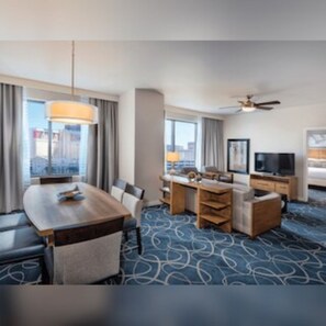 A hotel room with a dining table, chairs, a sofa, a TV, and a ceiling fan. - Club Wyndham Desert Blue (Las Vegas)