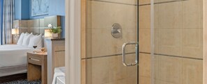 A hotel room with a bed, bedside table, lamp, and a shower area with a glass door. - Club Wyndham Desert Blue (Las Vegas)