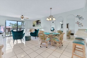 A spacious room with a dining area featuring a round table and chairs, a balcony with a view, and a ceiling fan. - Coastal Condo | Pool View + Heated Pool (St. Augustine)