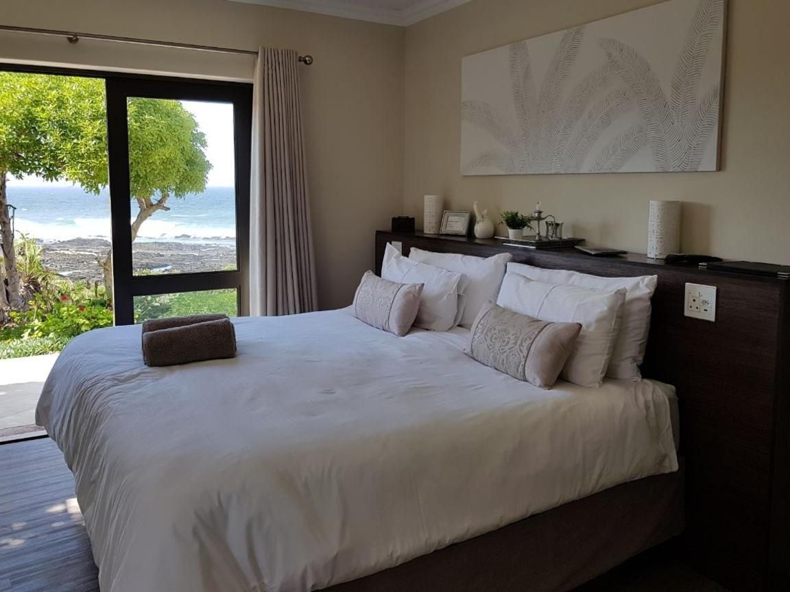 A bedroom with a large bed, a nightstand, and a view of the ocean.