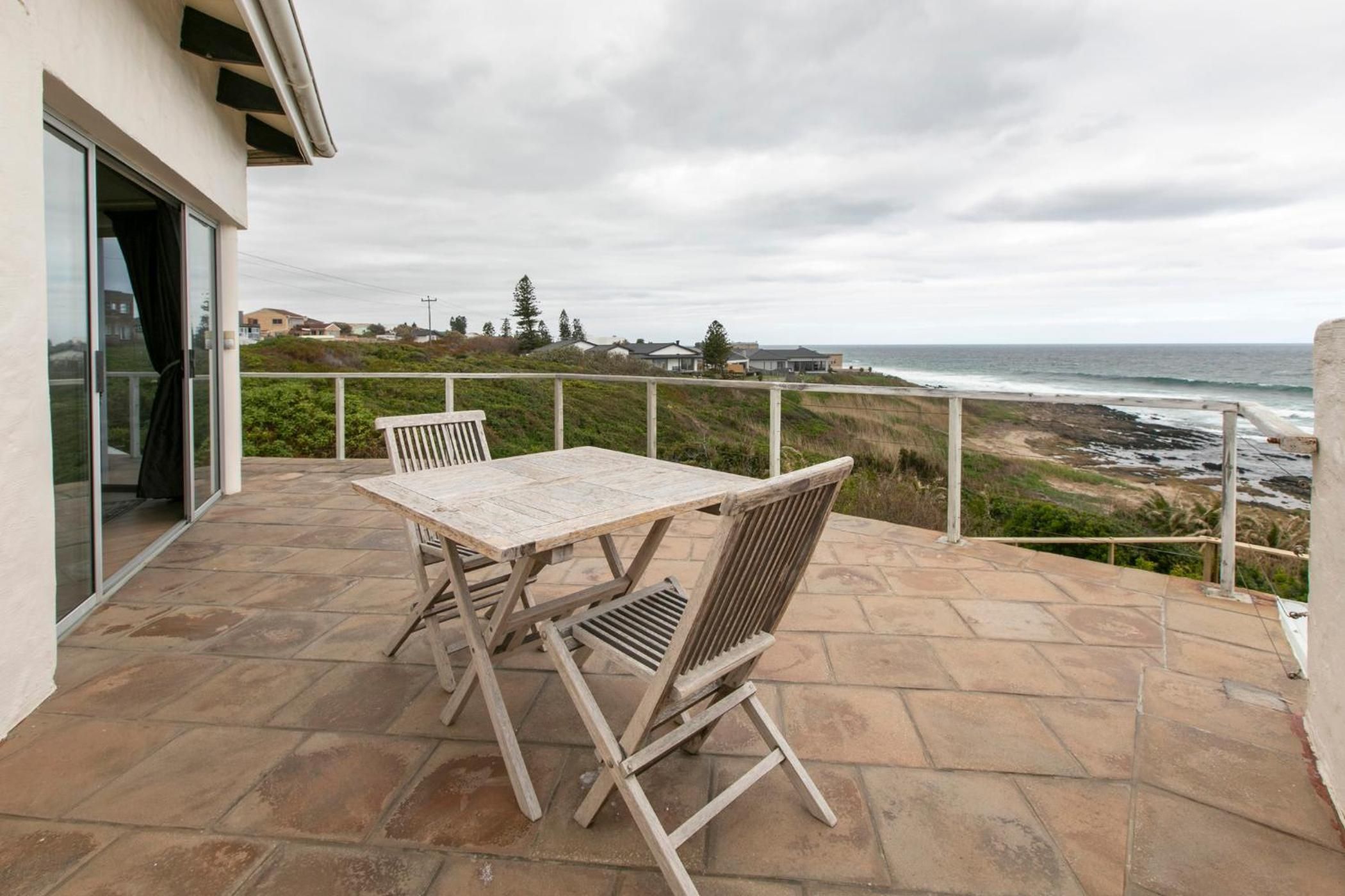 An outdoor patio with a table and chairs, overlooking a beach and ocean.