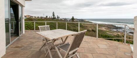 An outdoor patio with a table and chairs, overlooking a beach and ocean.