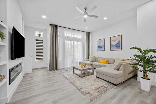 A modern living room with a flat-screen TV, a ceiling fan, a sofa set, and a coffee table. - Stylish 2BR/2.5BA | Garage | Near Downtown (Dallas)