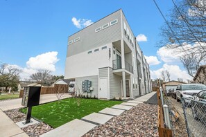 A multi-story residential building with a flat roof, a covered front porch, and a small front yard with artificial grass and a pathway. - Stylish 2BR/2.5BA | Garage | Near Downtown (Dallas)