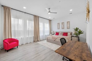 A modern bedroom with a bed, a red chair, a wooden table, and a ceiling fan. - Stylish 2BR/2.5BA | Garage | Near Downtown (Dallas)