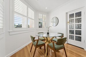 Een kamer met een ronde glazen tafel, omringd door vier stoelen, een potplant en een ronde spiegel aan de muur.