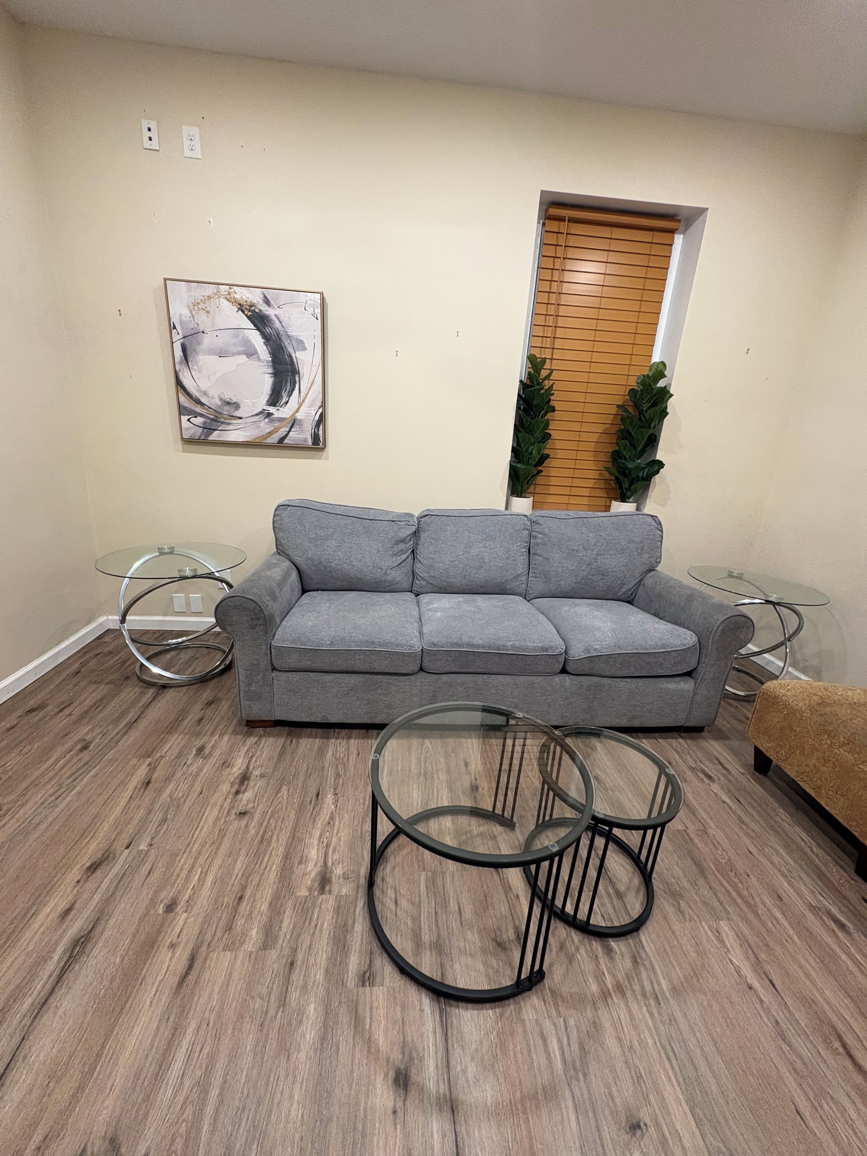 Una sala de estar con un sofá gris, una mesa de centro de cristal y piso de madera.