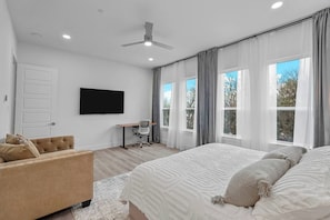 Quarto com cama grande, escrivaninha, cadeira e televisão na parede.