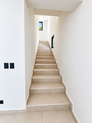 A staircase leading to a room with a window, white walls, and a light-colored floor. - Oceanview Villa · Private Pool Access · Panoramic Ocean Views (Garabito)