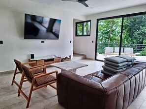 A modern living room with a flat-screen TV, a sofa, a dining table, and chairs. - Oceanview Villa · Private Pool Access · Panoramic Ocean Views (Garabito)