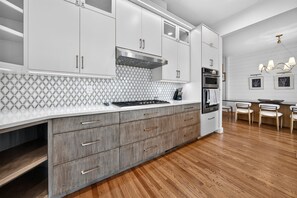 Eine moderne Küche mit weißen Schränken, einem Gasherd, einem Backofen und einem Essbereich mit Tisch und Stühlen.