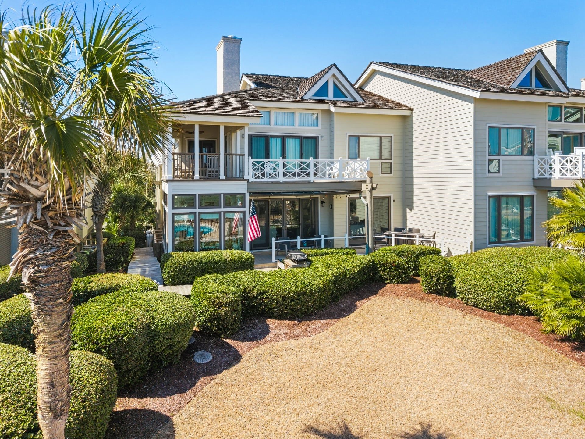 A two-story house with a covered patio, a swimming pool, and a well-maintained garden with palm trees and hedges.
