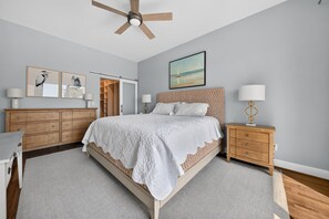 Ein Schlafzimmer mit einem großen Bett, einem Holzkleiderschrank, Nachttischen, einem Deckenventilator und Kunstwerken an den Wänden.