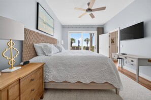 Une chambre à coucher comprenant un lit, une table de chevet, une lampe, un téléviseur et un ventilateur de plafond.