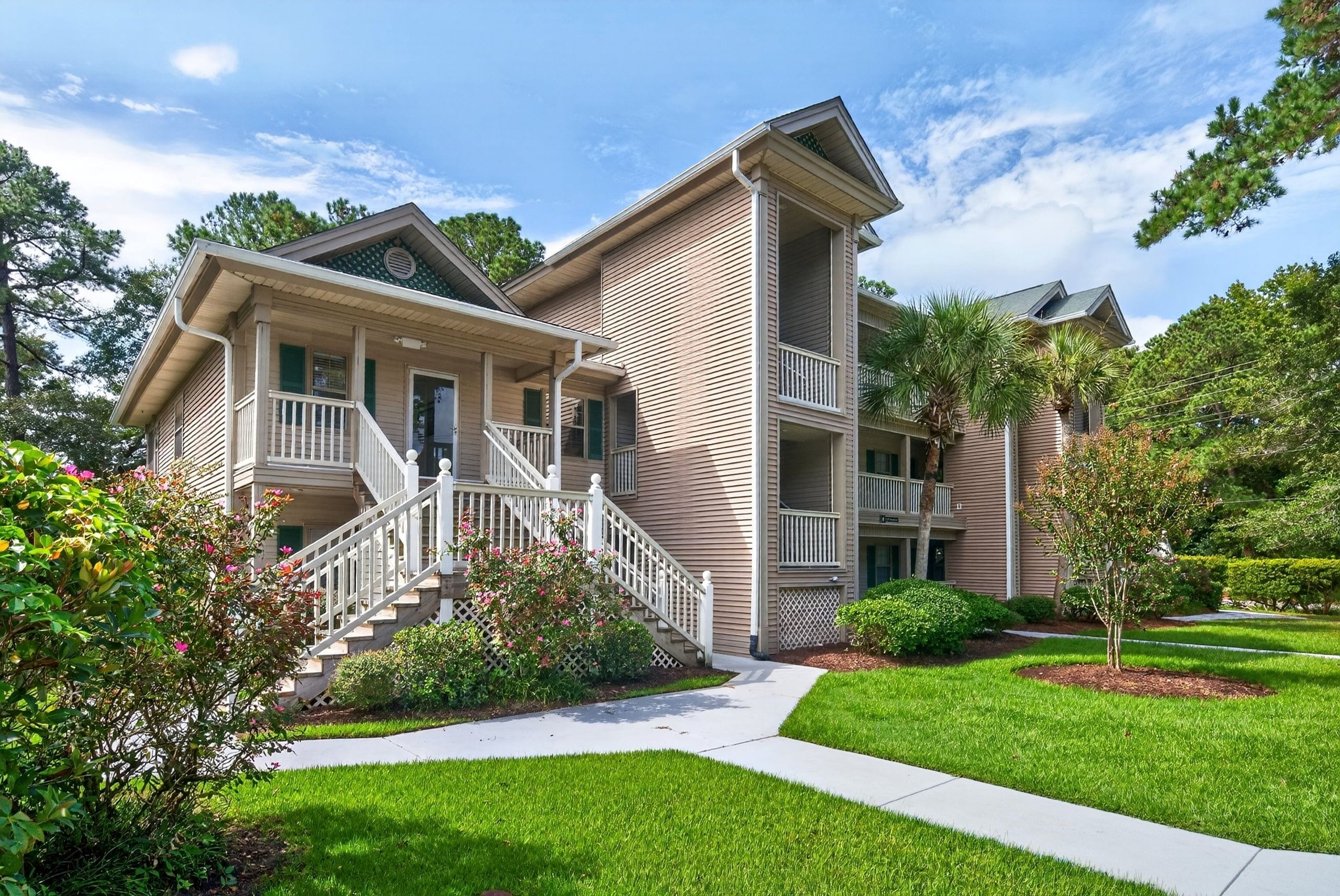 A two-story residential building with a covered front porch, a staircase leading to the entrance, and a well-maintained lawn.