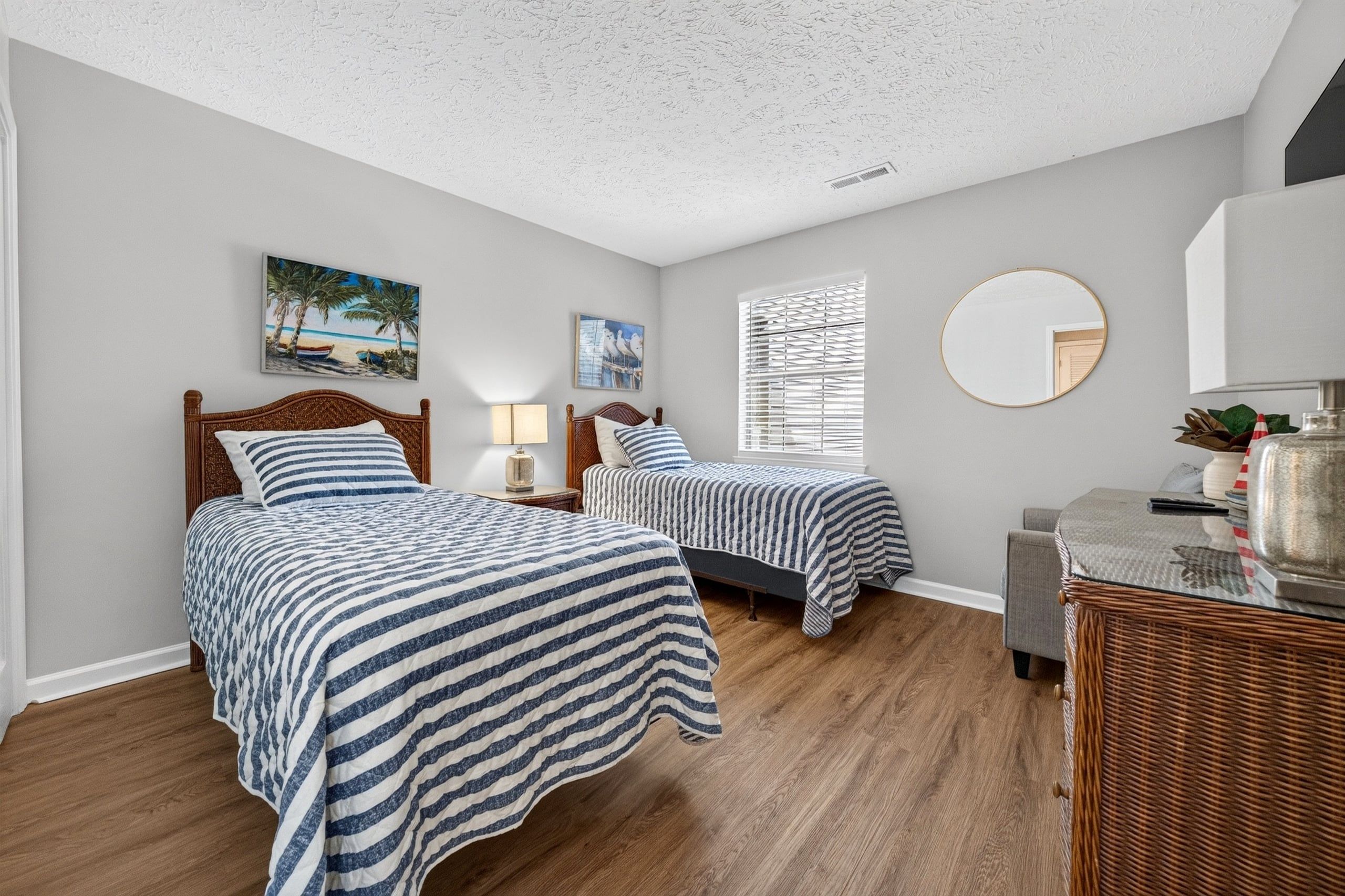 A bedroom with two beds, a round mirror, and artwork on the walls.