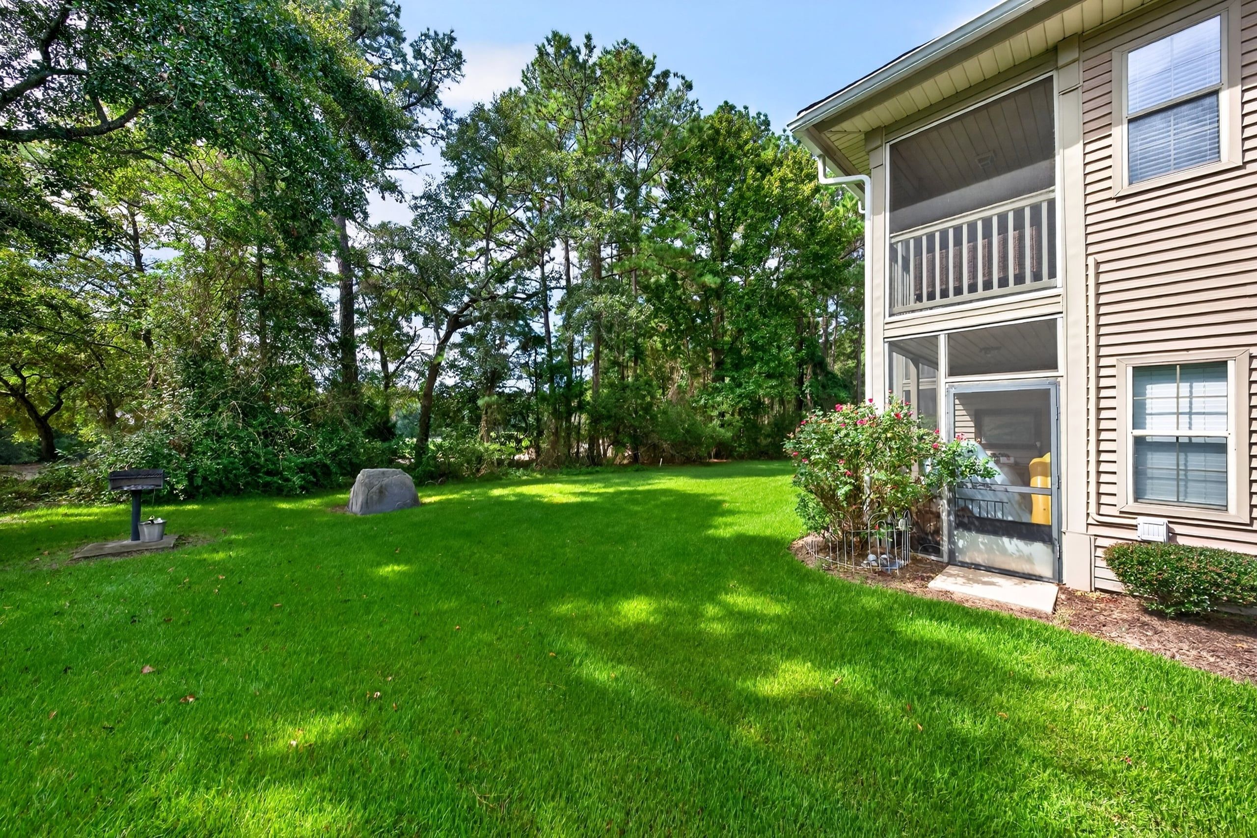 A residential property with a well-maintained lawn, a stone feature, and a two-story building with large windows.