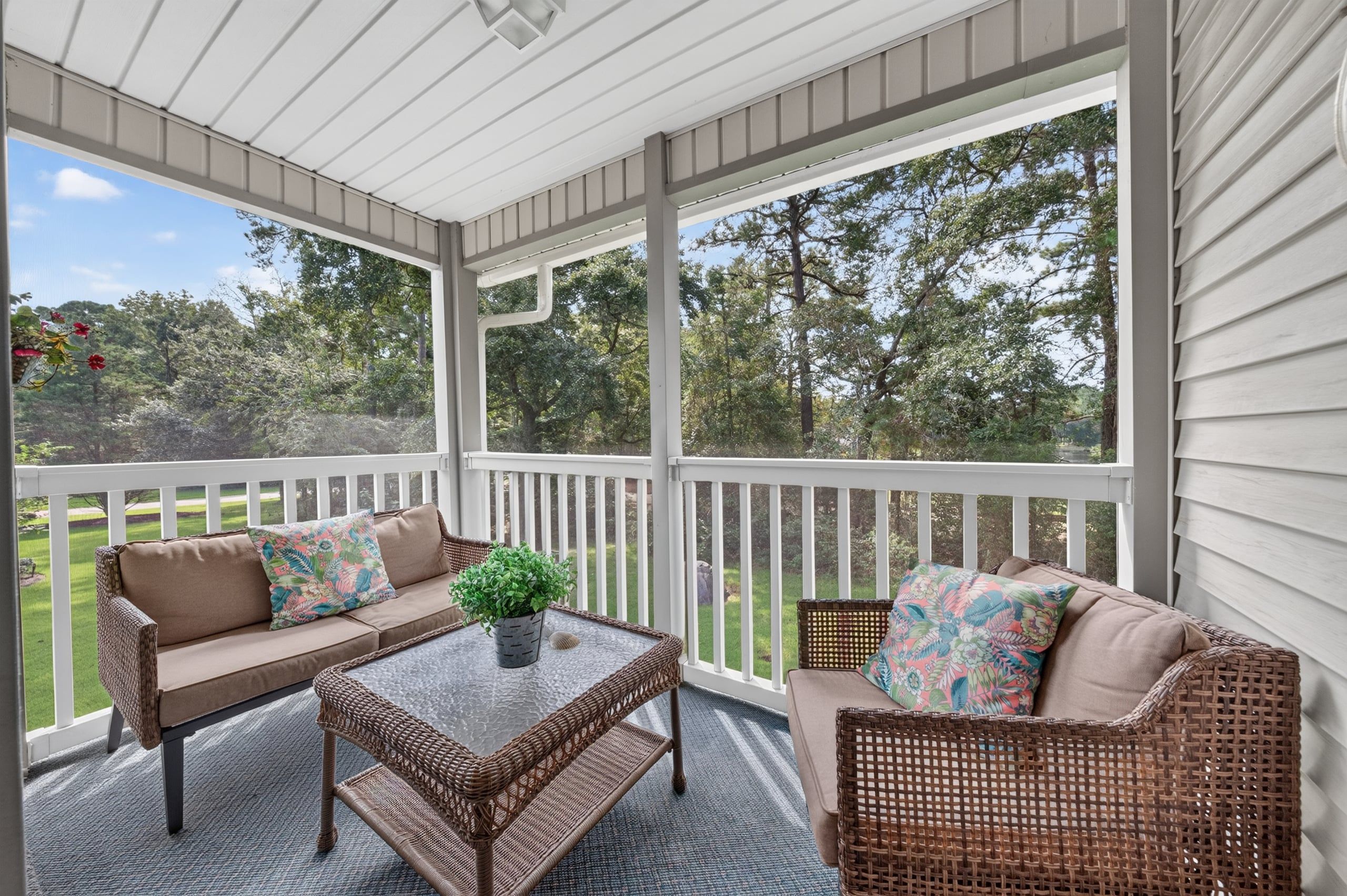 A covered porch with wicker furniture, a glass coffee table, and a potted plant.