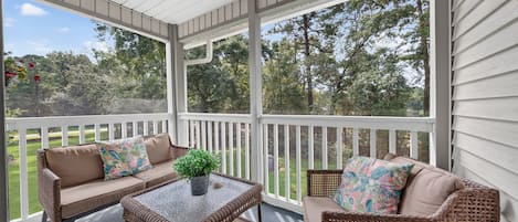 A covered porch with wicker furniture, a glass coffee table, and a potted plant.