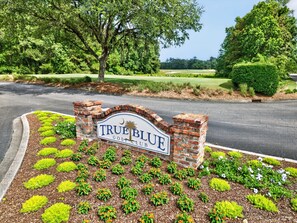 Placa de clube de golfe com um arco de tijolos, rodeada por canteiros de flores ajardinados.