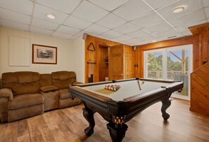 Ein Billardtisch in einem Raum mit Holzboden, einem braunen Sofa und einem gerahmten Bild an der Wand.