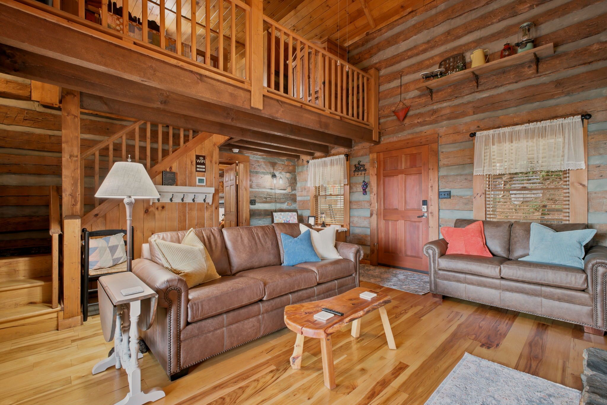 L’intérieur d’une cabane en rondins, avec un escalier en bois, deux canapés en cuir, une table basse en bois et une lampe.