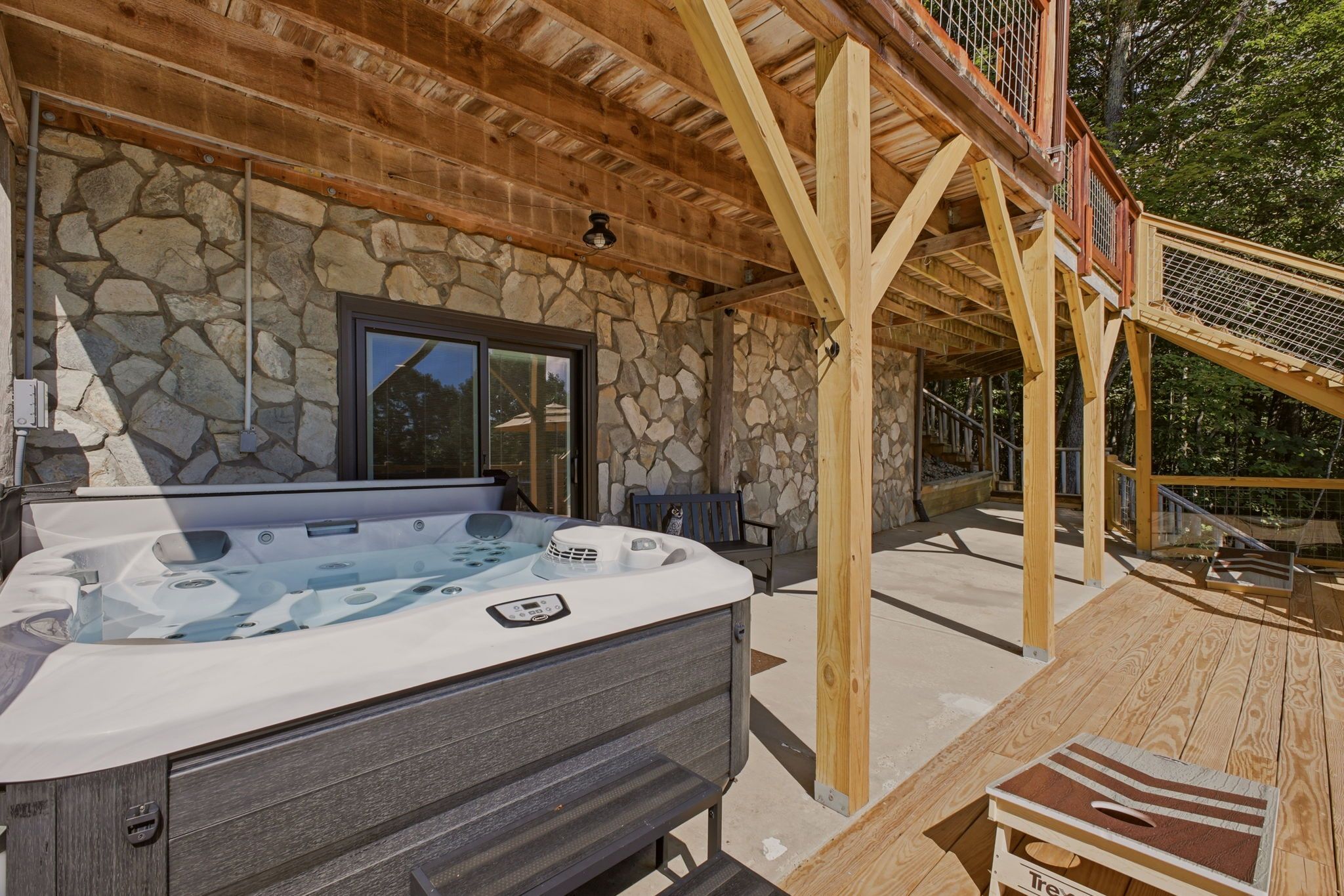 Un bain à remous installé sous une pergola en bois, avec des murs en pierre, une fenêtre et une terrasse.