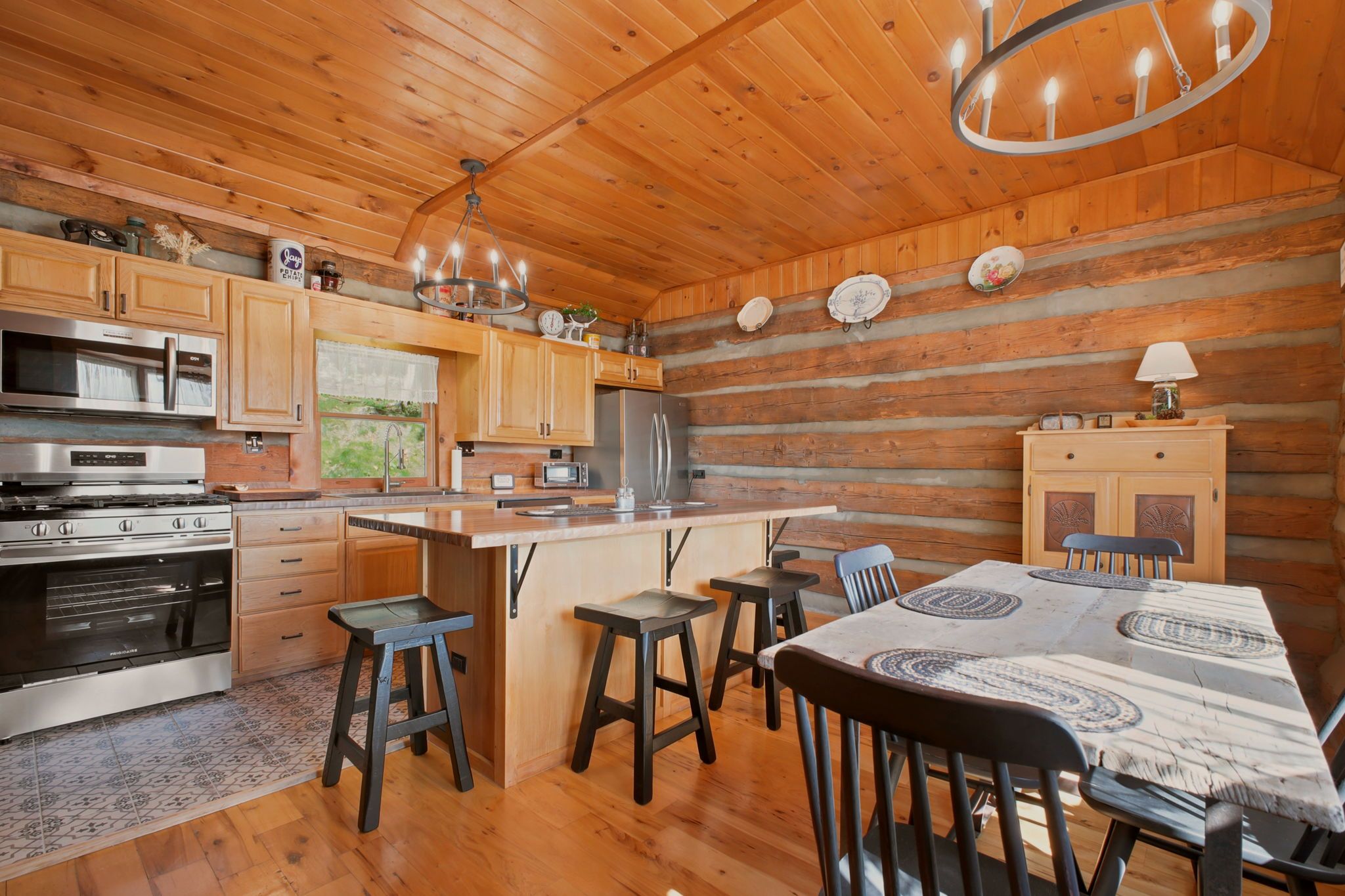 A log cabin-style kitchen with wooden cabinets, a stainless steel refrigerator, a stove, and a dining area with a table and chairs.