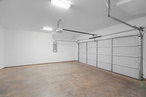 A garage with a concrete floor, white walls, and a white garage door. - Cozy 2BR Townhome | Garage | Near Downtown (Dallas)