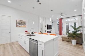 A modern kitchen with white cabinetry, a central island, and a dining area with orange chairs. - Cozy 2BR Townhome | Garage | Near Downtown (Dallas)