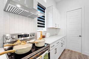 A modern kitchen with white cabinetry, a stainless steel stove, and a window above the sink. - Cozy 2BR Townhome | Garage | Near Downtown (Dallas)