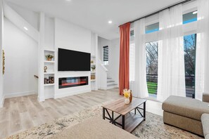 A modern living room with a flat-screen TV, fireplace, and a sofa. - Cozy 2BR Townhome | Garage | Near Downtown (Dallas)