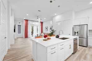 A modern kitchen with white cabinetry, a stainless steel refrigerator, and a central island with a sink. - Cozy 2BR Townhome | Garage | Near Downtown (Dallas)