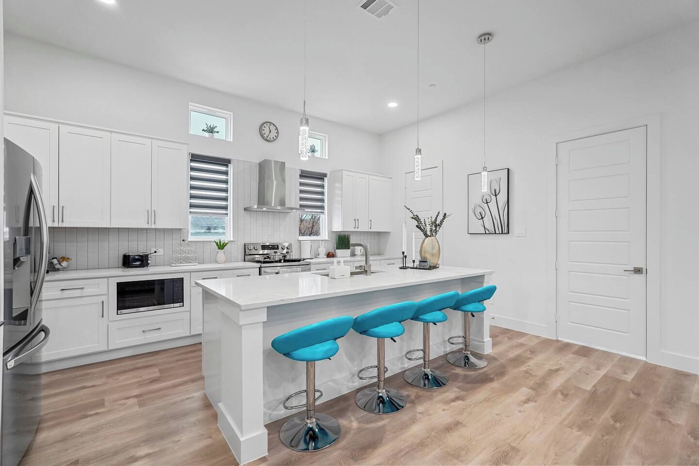 A modern kitchen with white cabinetry, a central island with bar stools, stainless steel appliances, and pendant lighting.